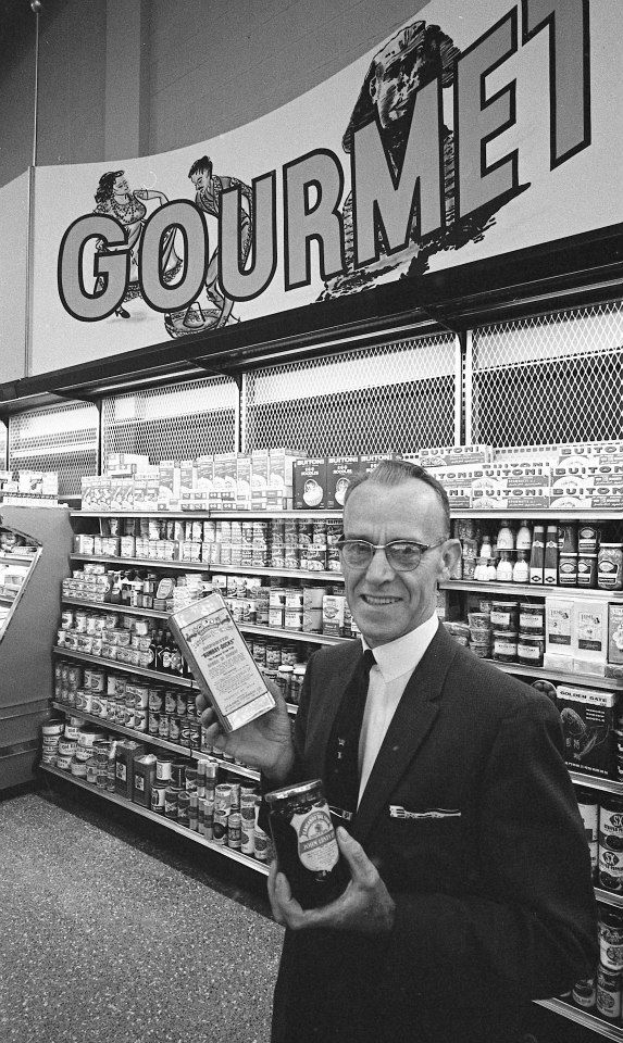 George P. Pearce manager of the Gourmet Foods department. Mr. Pearce is holding a can of Bombay Ducks (lizardfish) and Kangaroo Tail soup.